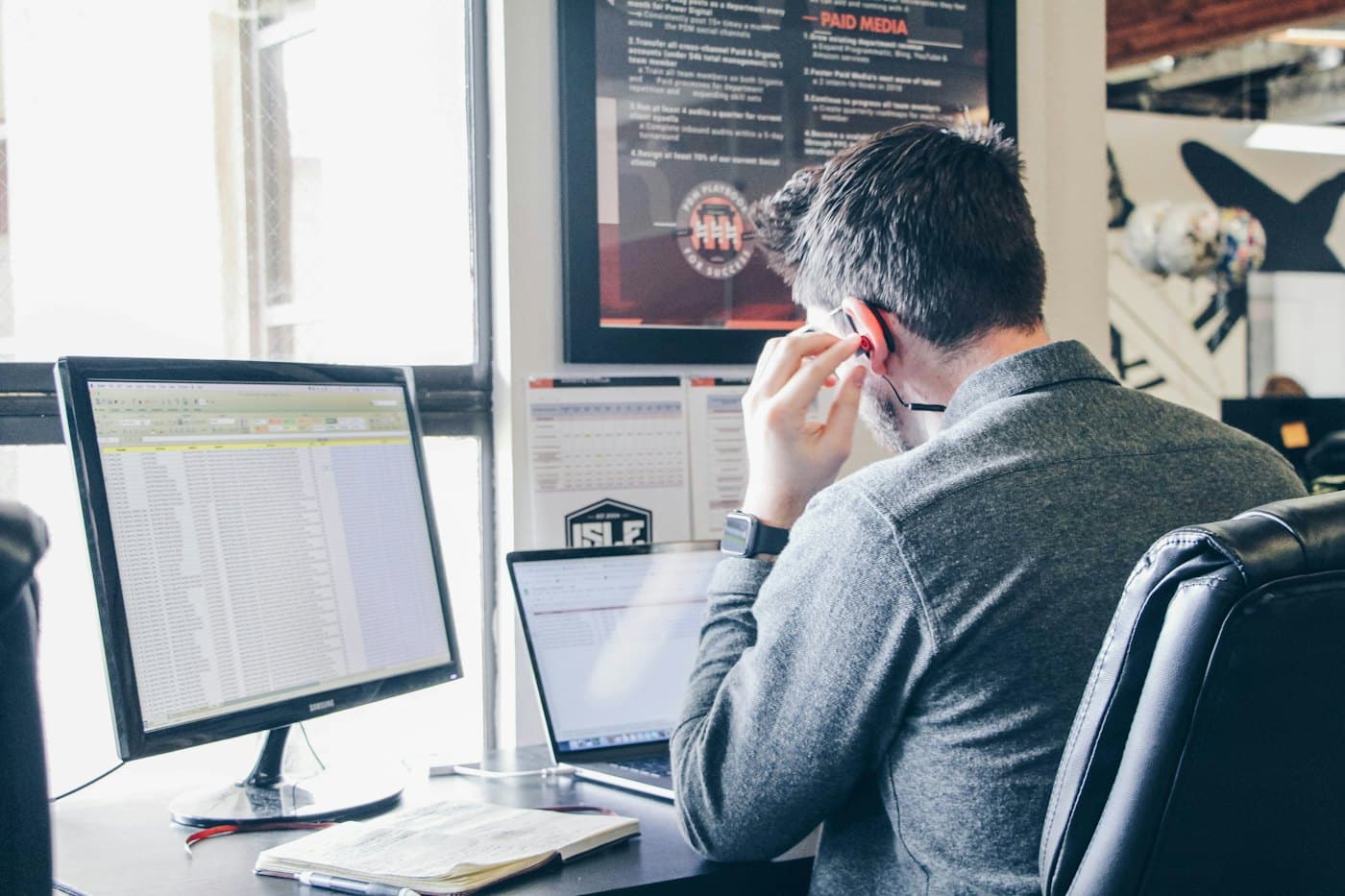 Dispatcher on a call at his desk, an order spreadsheet open on the monitor